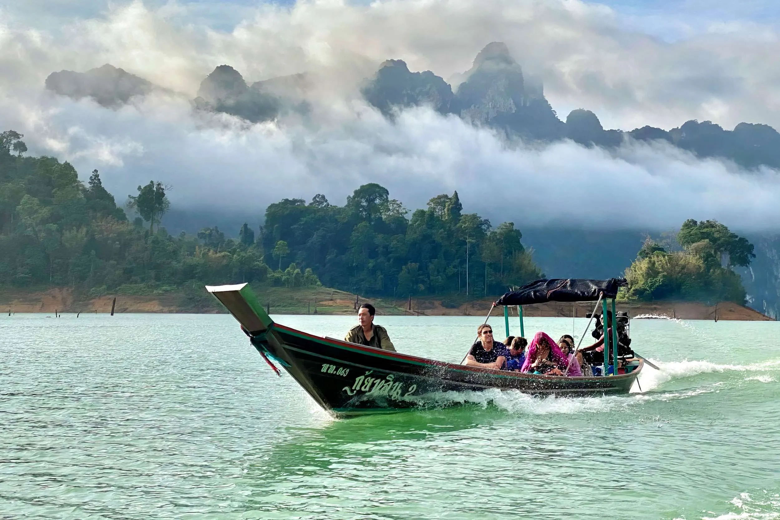 A long tail boat makes its way across the Cheow Lan lake in the Khao Sok national park, Thailand. The mist covered karst mountains behind add to the drama.